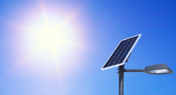 A solar panel facing towards a bright sun and powering a street lamp